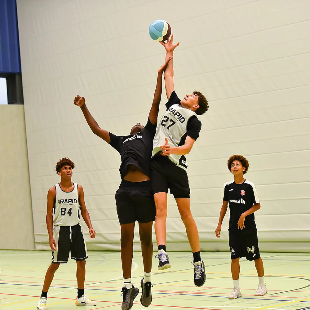Two students competing for a jump ball during a FooBaSKILL basketball session